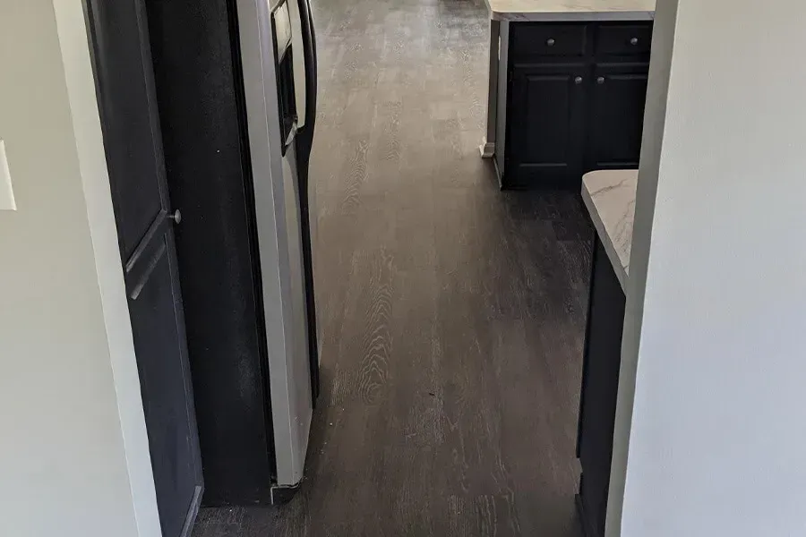 Narrow kitchen hallway with dark wood floors, a black refrigerator, and dark cabinets.