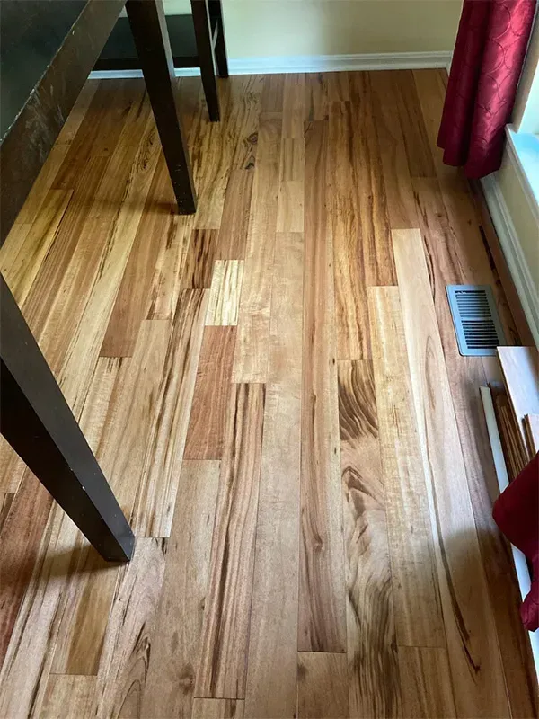 Wooden floor with varying shades of brown. A table leg is in the top left, a red curtain and vent are on the right.