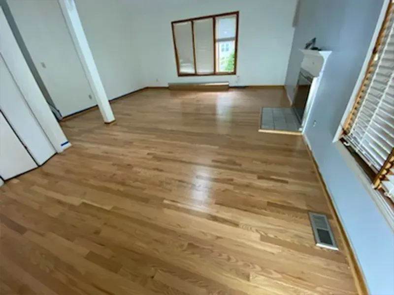 Wooden floors in an empty room, a window, and a fireplace with a gray tile hearth.