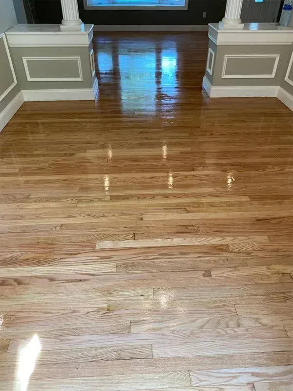 Shiny hardwood floors reflect light in an entryway, framed by white columns and light green walls.