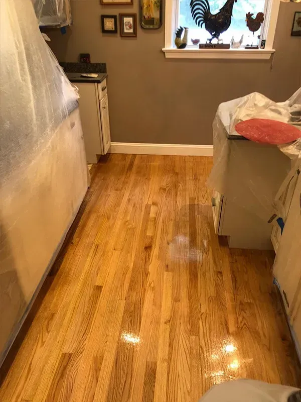 Wooden kitchen floor with cabinets on both sides, some covered with plastic.