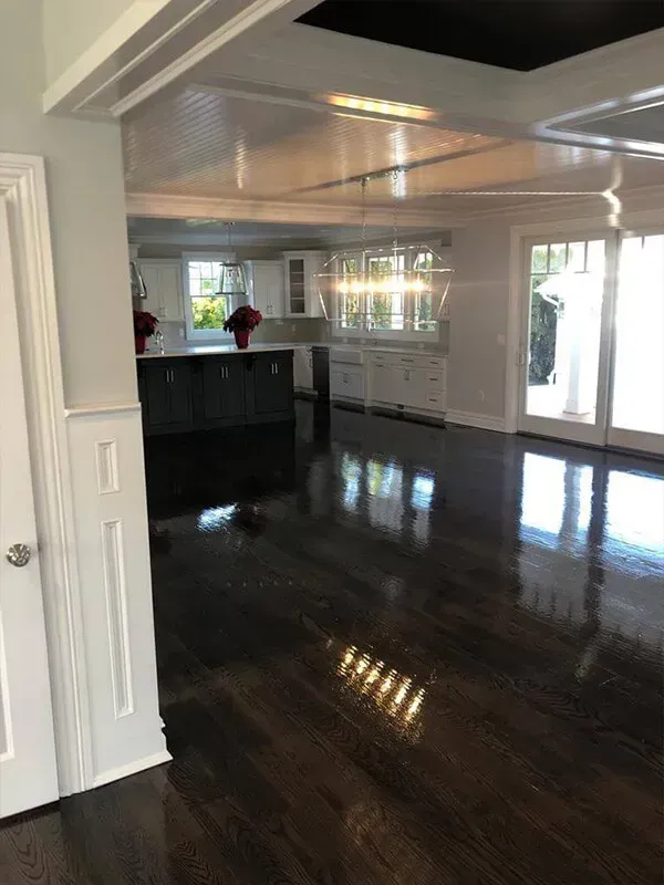 Dark hardwood floors reflect light in an open-concept living space, leading to a kitchen with white cabinetry and a black island.