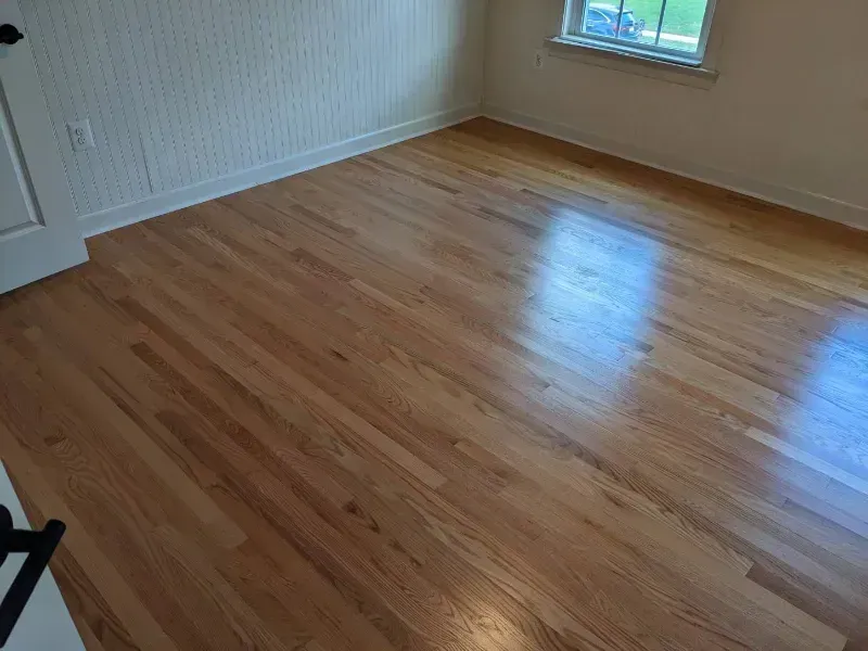 Hardwood floor in a room with a white wall, a door, and a window, reflecting light.