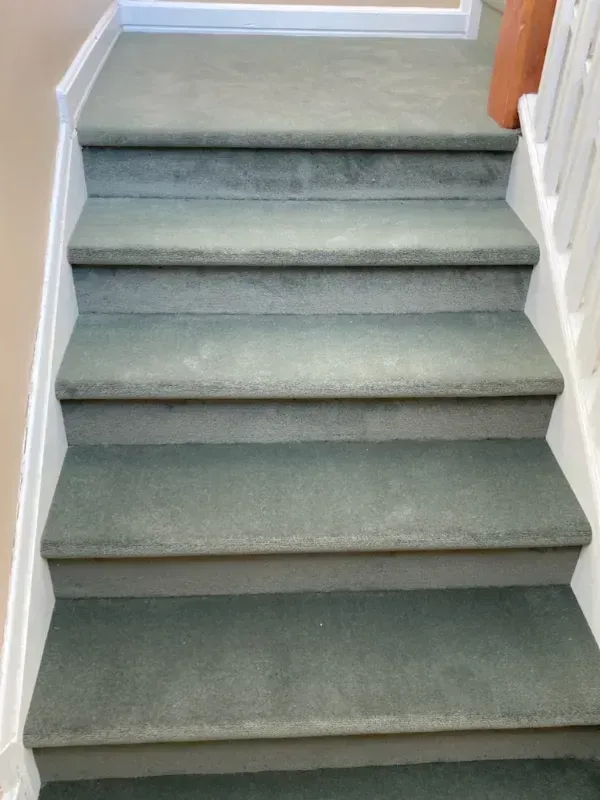 A flight of carpeted stairs with a green hue. White banister on the right and a doorway at the top.