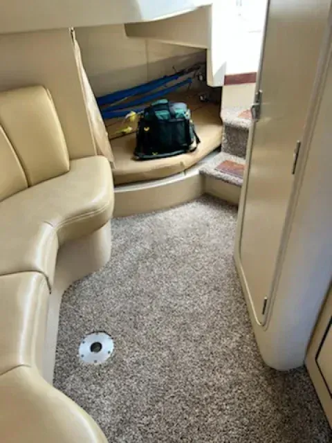 Interior of a boat cabin. Tan carpet, beige leather seating, a step up to another area with a toolbox.