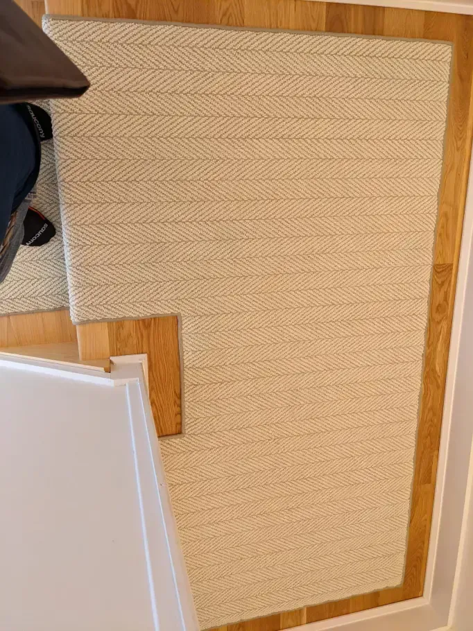 Beige woven rug with a brown border on hardwood flooring