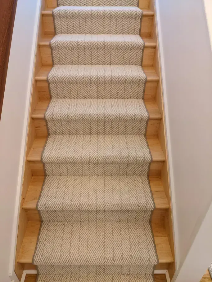 Staircase with light-colored carpet runner on wooden steps. The walls are white.