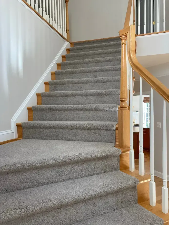 Carpeted staircase with wooden handrails. Light gray carpet covers the stairs, wooden trim and railings are present.