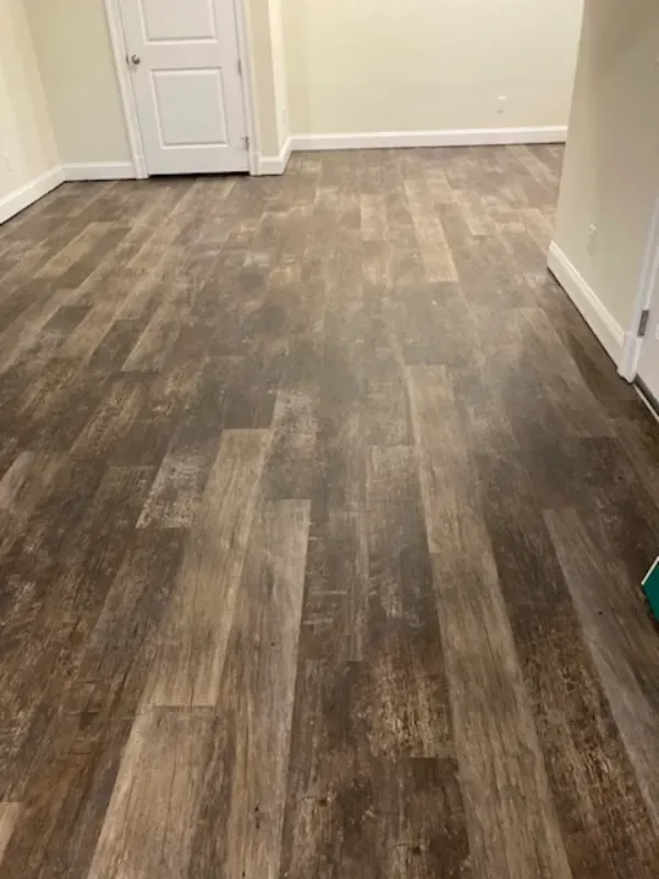 A room with wood-look flooring. A white door and off-white walls are visible.