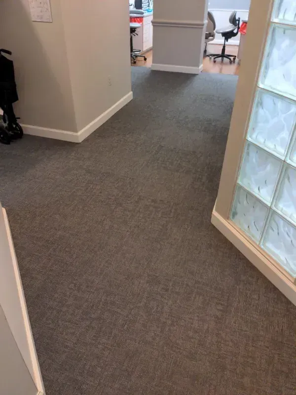 Hallway with gray carpet and off-white walls. A glass block window is on the right. 