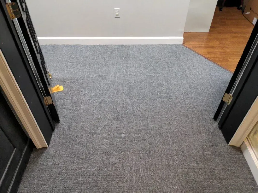 Open black door frames leading into a room with gray carpet and a white baseboard. 