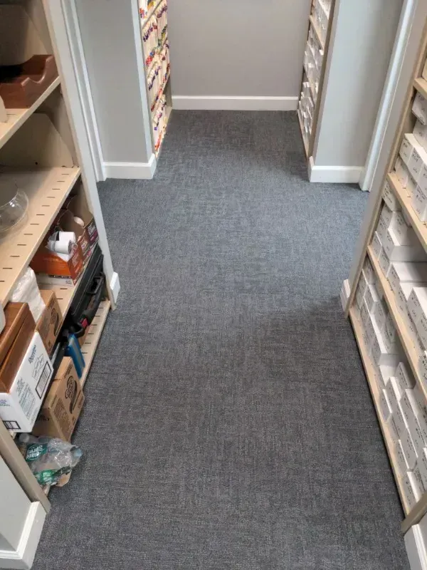 A narrow storage room with gray carpet, shelves on either side, and items stored on them.