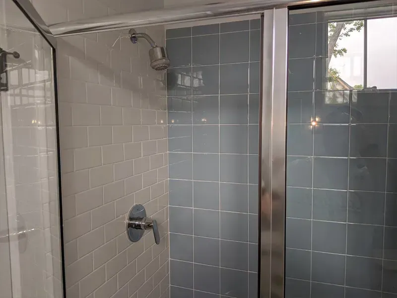 Shower stall with blue and white tiles, glass doors, and silver fixtures. The showerhead and handle are visible.