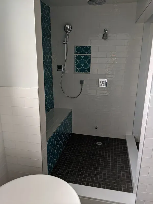 A newly renovated shower with teal accent tiles and dark floor tiles. The shower has a built-in bench and a rain shower head.