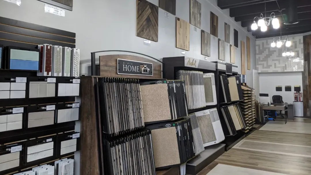 Interior of a tile store, displaying various tile samples on walls and shelving. Beige, brown, and patterned tiles are prominently featured.