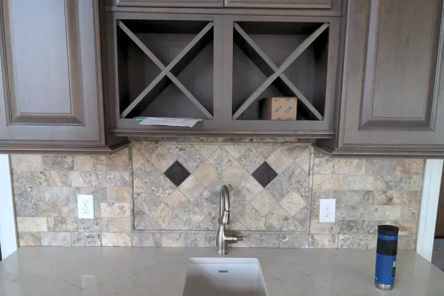Kitchen counter with backsplash tile, cabinets, and a faucet. The backsplash has a diamond pattern.