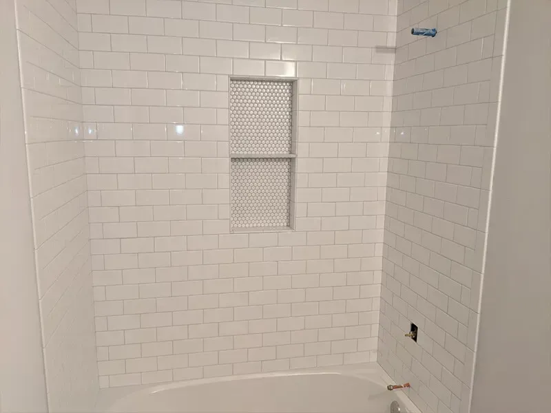 White tiled shower with a built-in shelf, featuring a curved bathtub and a silver showerhead.