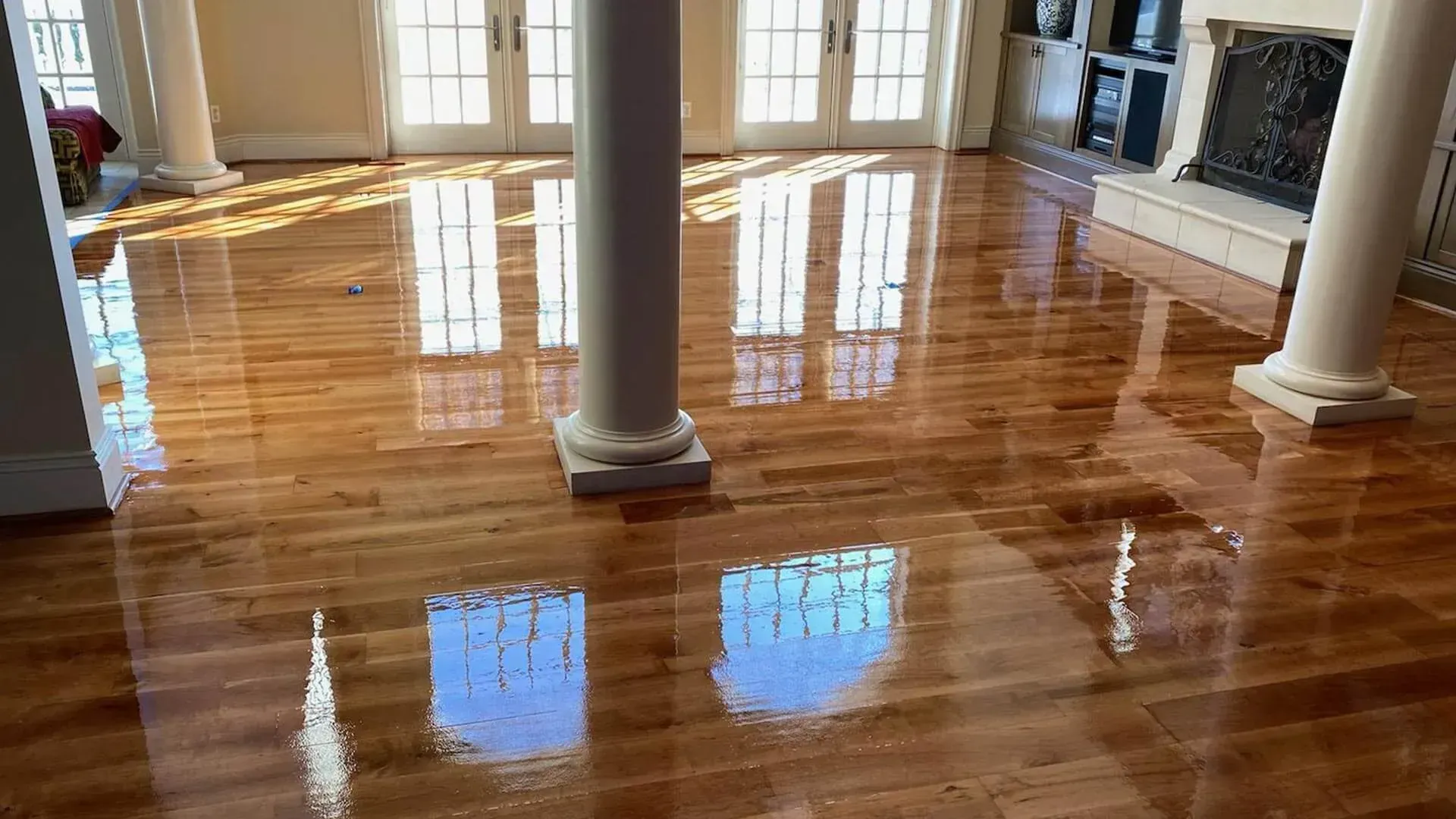 Polished hardwood floor reflecting light from windows and columns. Bright interior with a fireplace visible in the background.