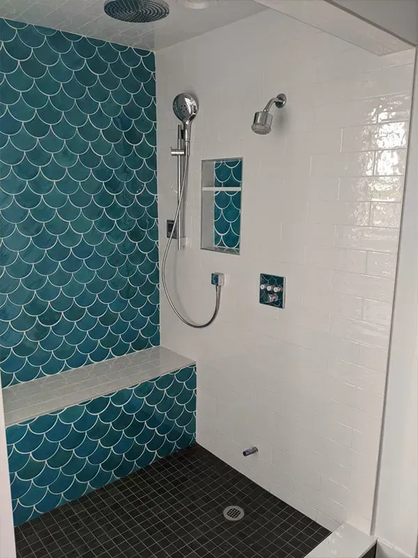 A modern shower with teal fish-scale tile on the back wall and a built-in bench. White subway tile and dark floor tile complete the design.
