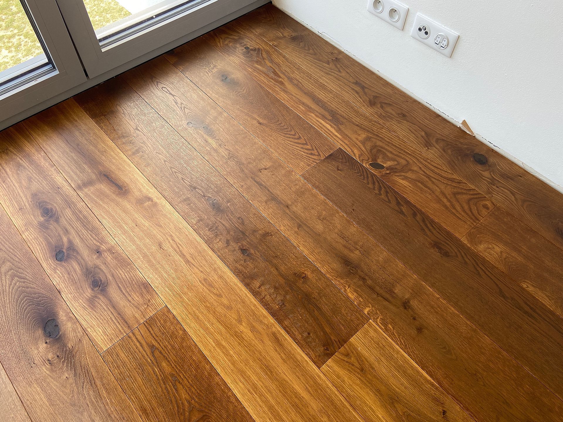 Wooden floorboards in various shades of brown and tan are angled towards a window. The floor has a glossy finish.