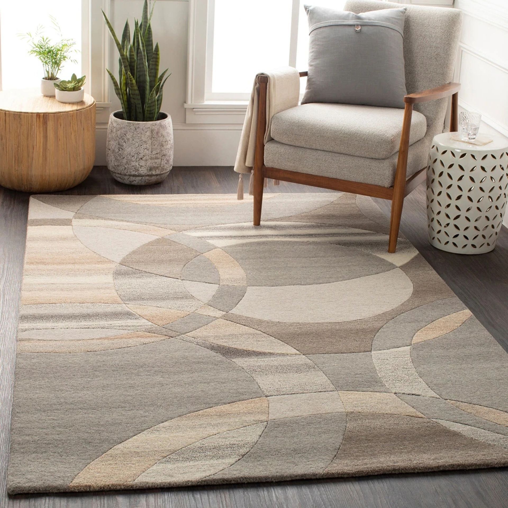 A living room scene featuring a geometric patterned rug, armchair with pillow, and side tables. Neutral tones and modern style.
