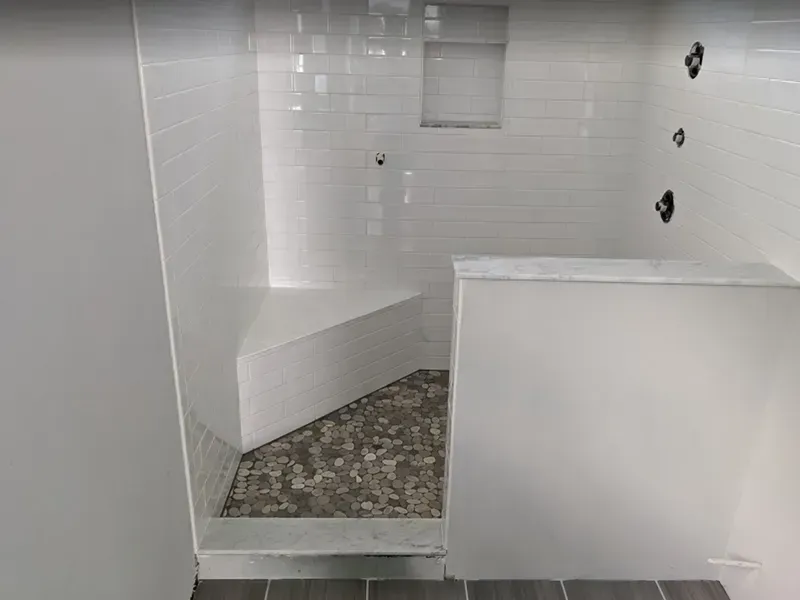 A white-tiled shower with a built-in bench and mosaic floor. Three black showerheads are mounted on the wall.
