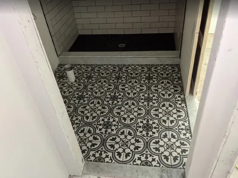 A newly tiled bathroom floor with a black and white patterned design, leading to a shower with a dark floor and white brick-like tiles.