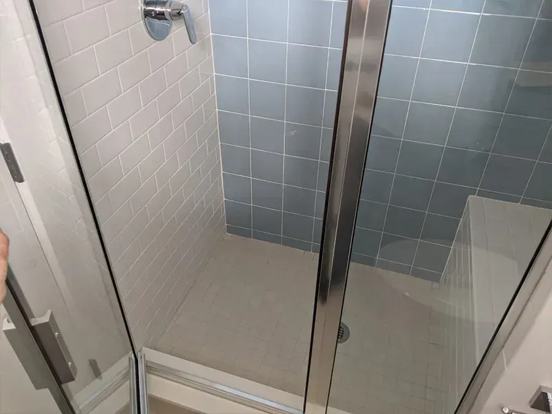 Shower stall with white and blue tiles. Glass door is open, showing the interior.