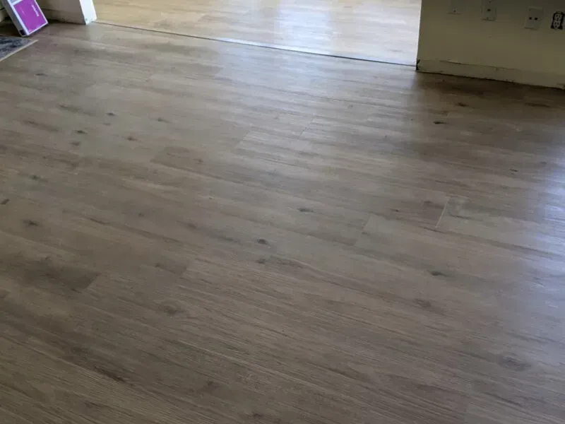 Light brown wood-look flooring in a room. Flooring extends to another area in the background.