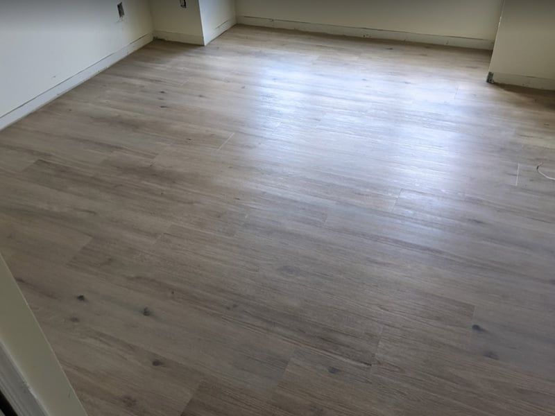 Light brown hardwood floor filling a room, with white walls in the corners.