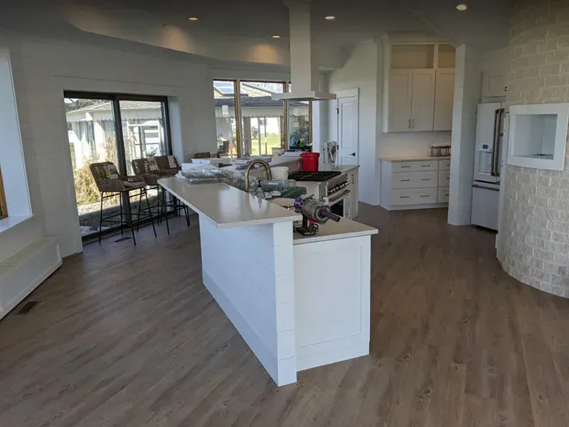 Modern kitchen with a white island, stainless steel appliances, and large windows. 