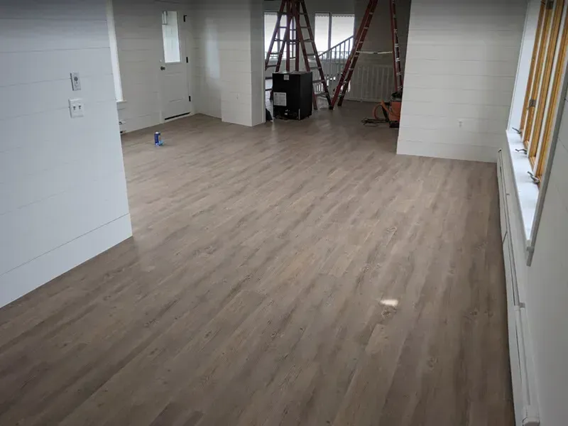 Newly installed wood flooring in a bright, open room with white walls and a glimpse of a doorway and staircase.