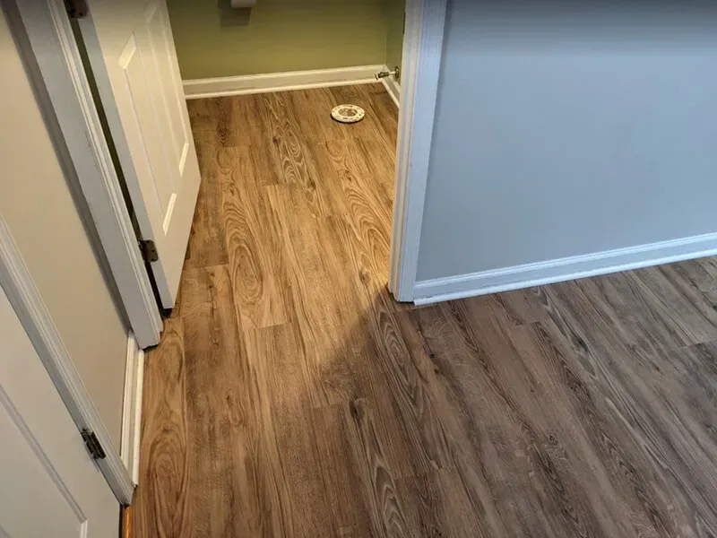A doorway with wood-look flooring. The floors are a warm brown and transition into a green-painted space.
