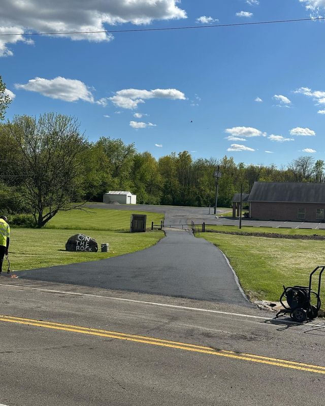Paved path through a grassy park toward a building under a blue sky with scattered clouds.