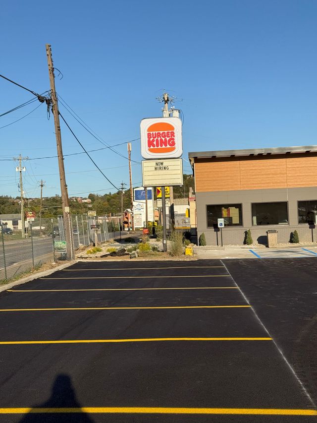 Brick building and dark gray wall beside a taped-off parking lot with orange cones on a sunny day