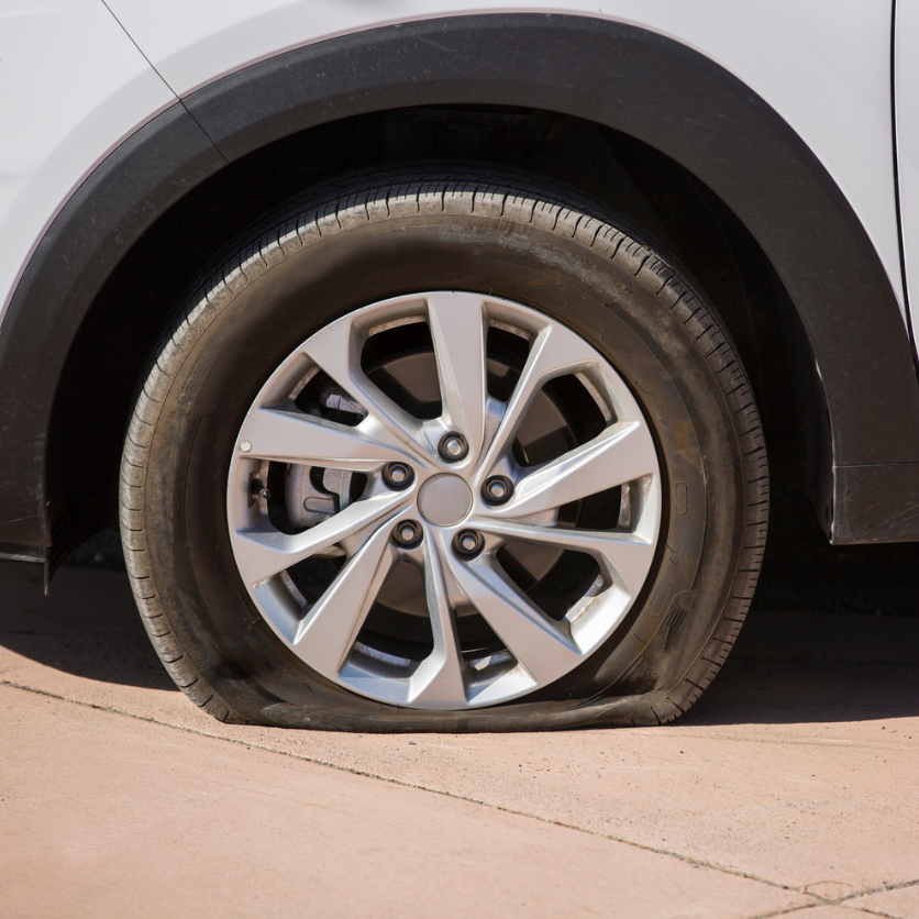 Flat car tire on pavement. Gray car with black wheel well.