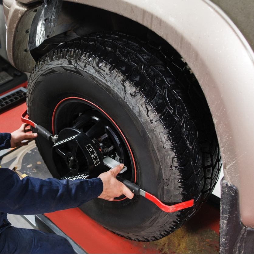 Wheel alignment being performed on a vehicle. A technician adjusts the tire with tools.
