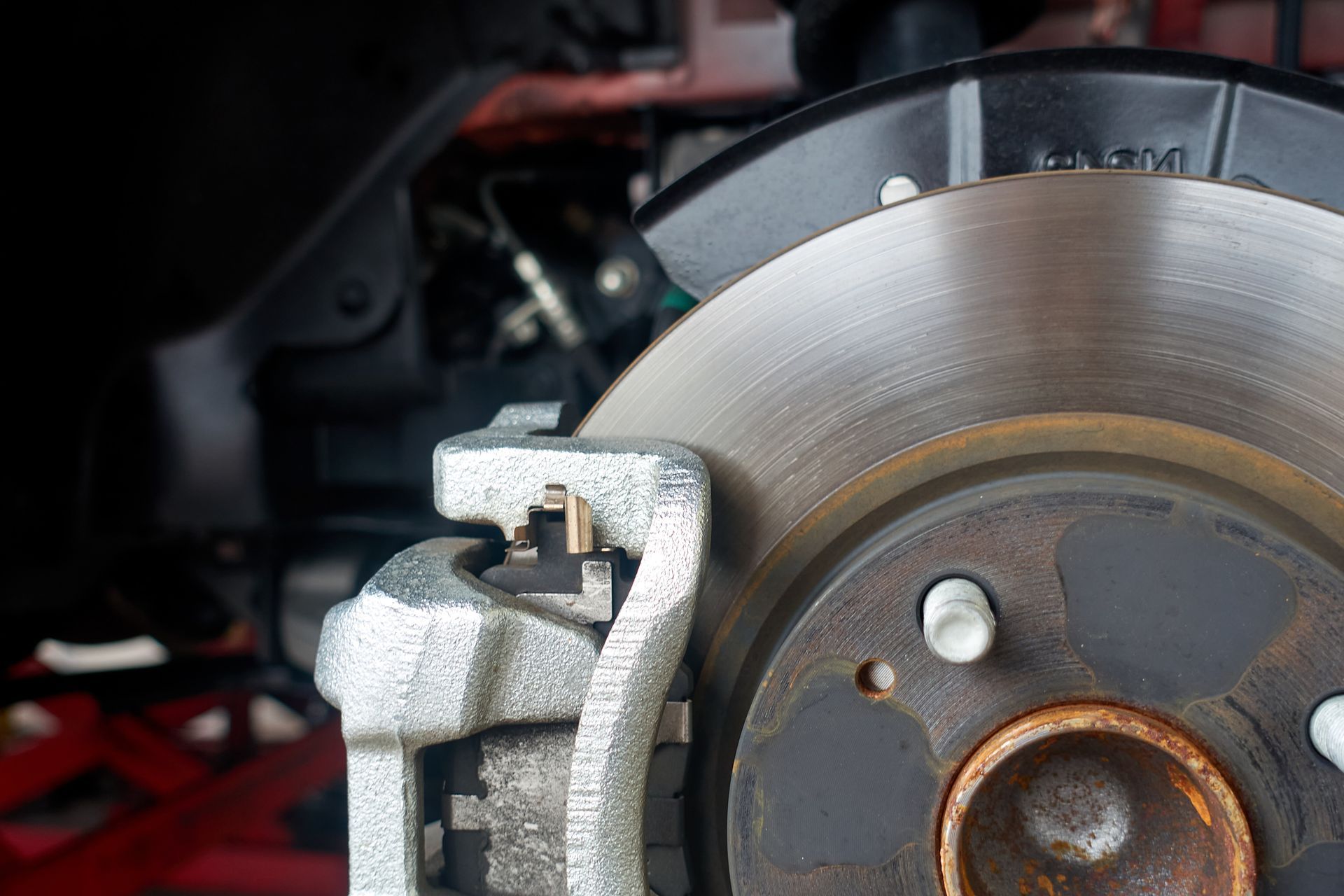 Close-up of a car's brake disc and caliper. Silver disc, rusty hub, and silver caliper.