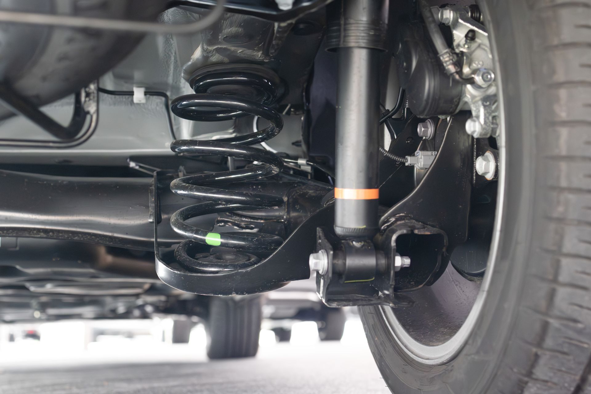 Close-up of a car's rear suspension with a black coil spring, shock absorber, and wheel.
