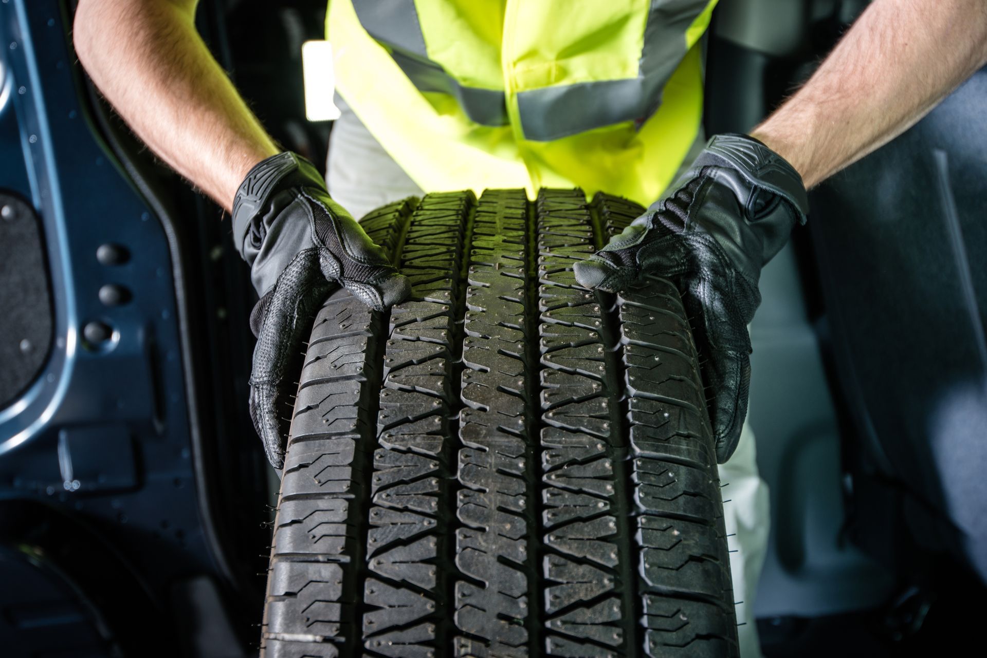 Person wearing gloves and a safety vest lifting a tire out of a vehicle.