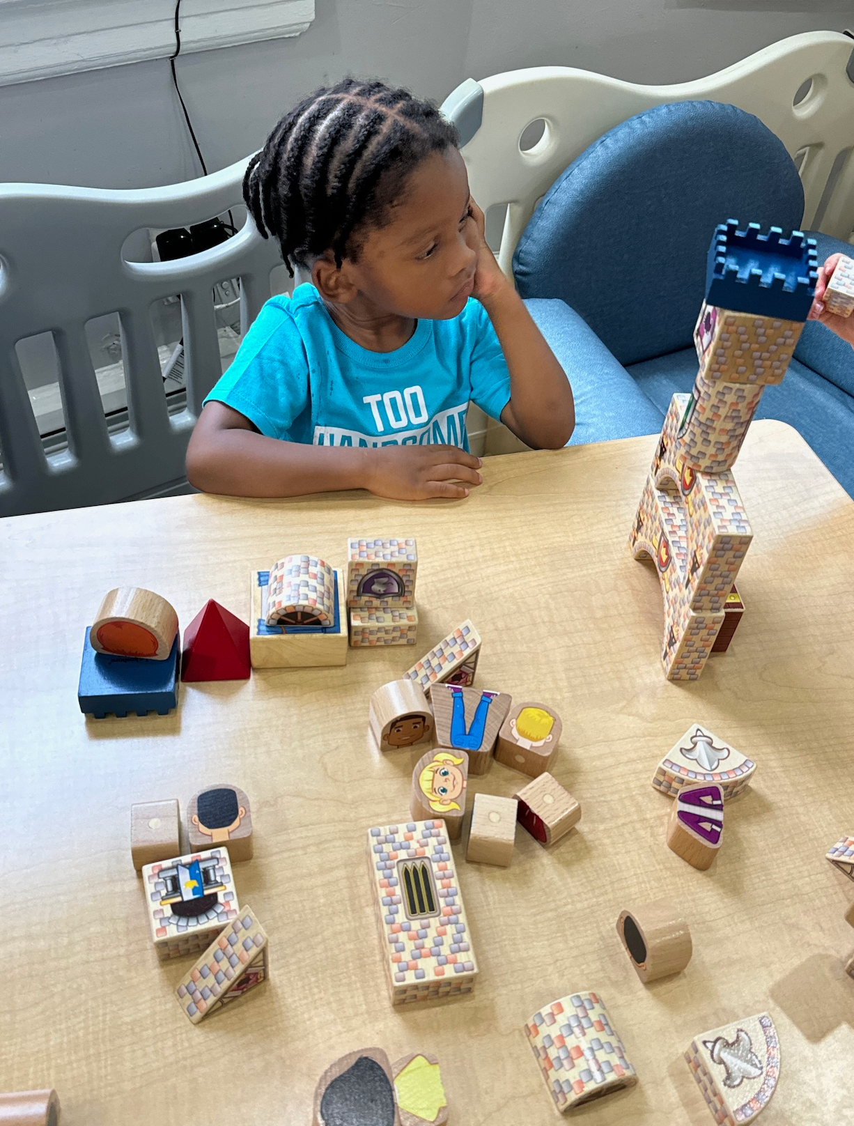 A little girl is sitting at a table playing with wooden blocks.