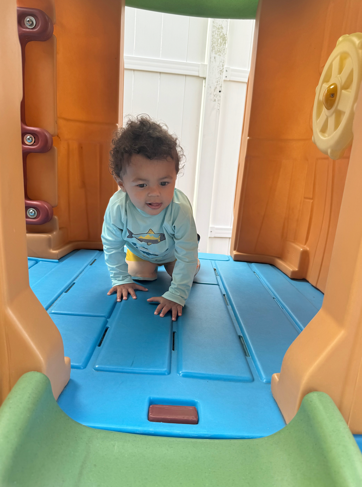 A baby is crawling on the floor of a playhouse.