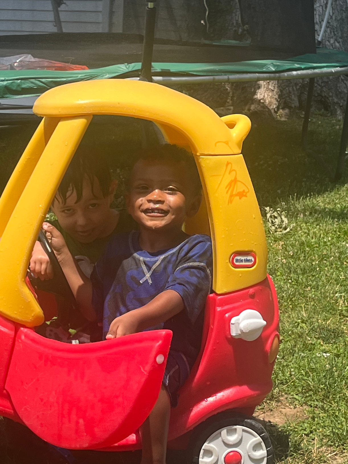 Two children are sitting in a little tikes car.