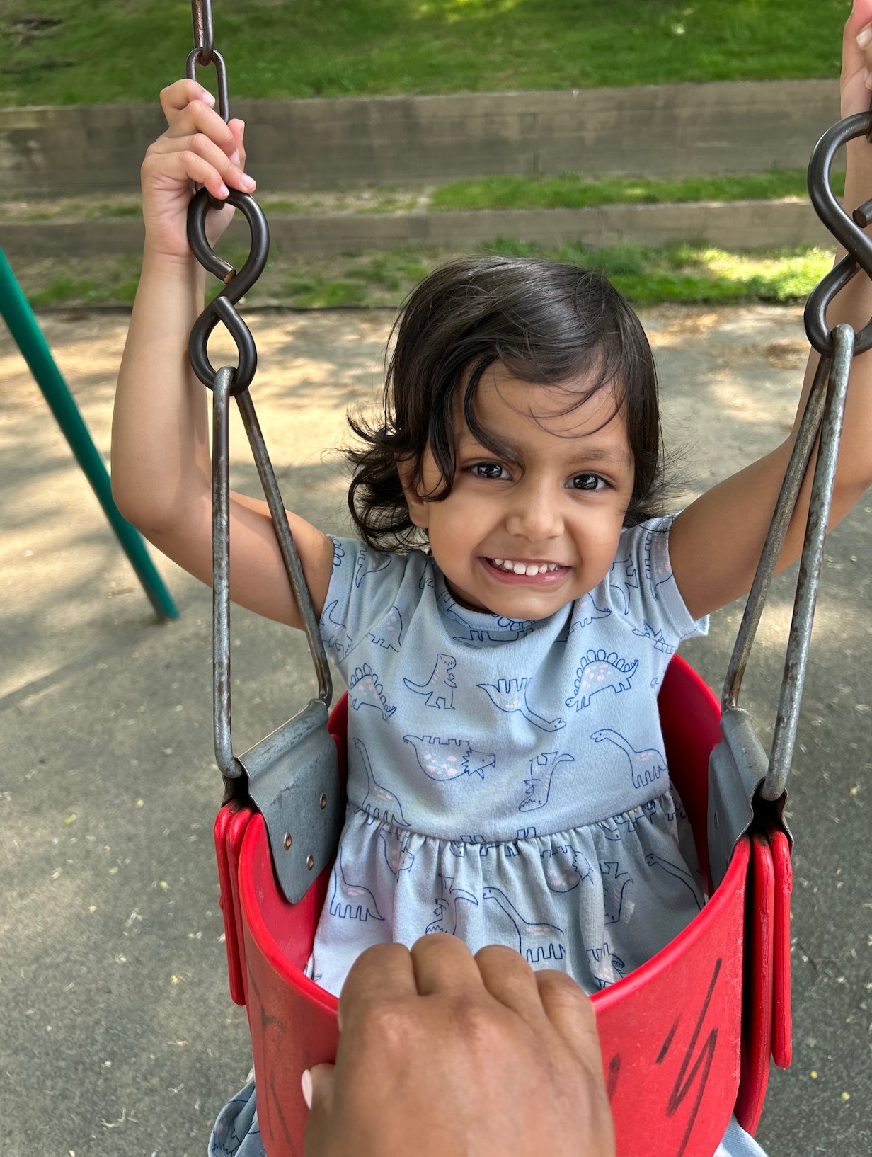 A little girl in a blue dress is sitting on a red swing
