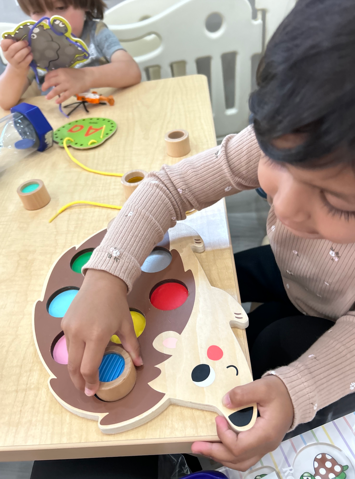 A child is playing with a wooden hedgehog toy.