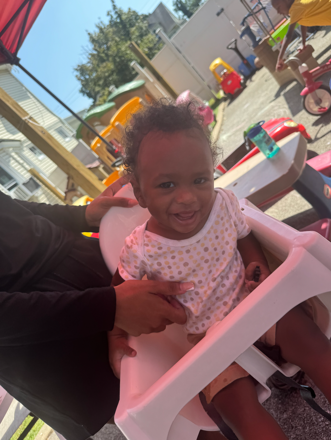 A baby is sitting in a high chair outside and smiling.
