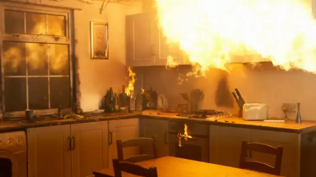 A kitchen engulfed in flames; cabinet, stove, and window are burning. Fire spreads rapidly.