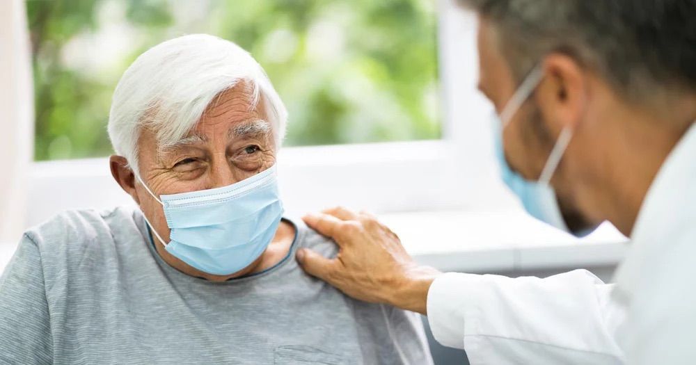 An elderly man wearing a face mask is talking to a doctor.