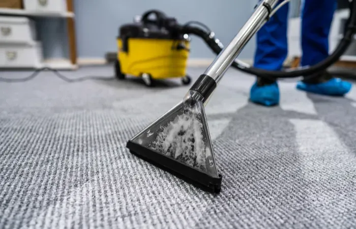 A person is removing water from a carpet with a vacuum cleaner.