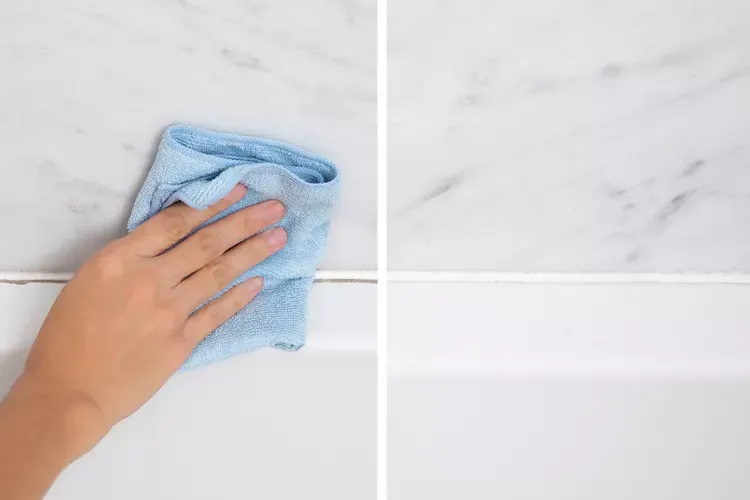A person wiping a shower wall with a blue rag